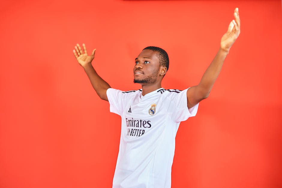 An enthusiastic football fan celebrating with arms raised in a jersey against a red background.