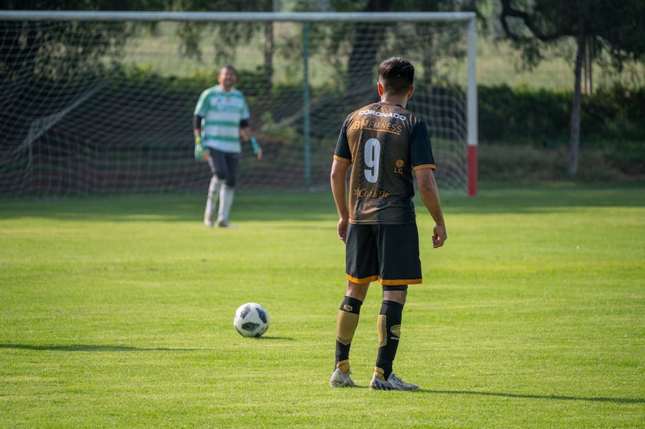 Soccer player in action preparing for a penalty kick on a sunny day in a green field.