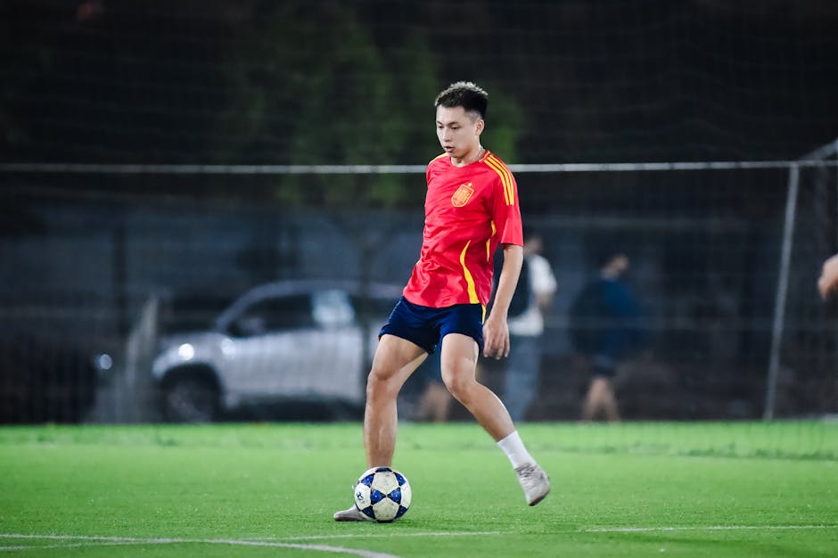 Athlete in a red jersey plays soccer at night on a field in Hanoi, Vietnam.