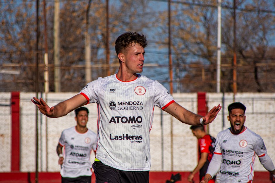 Soccer team members celebrate a goal during an outdoor match on a sunny day.