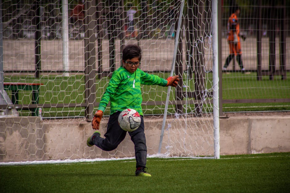 A young goalkeeper in action, kicking a soccer ball on the field during a match.