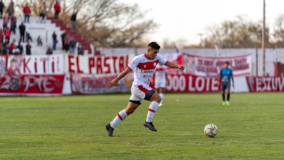 A football player in action on the field during an outdoor match with spectators in the background.