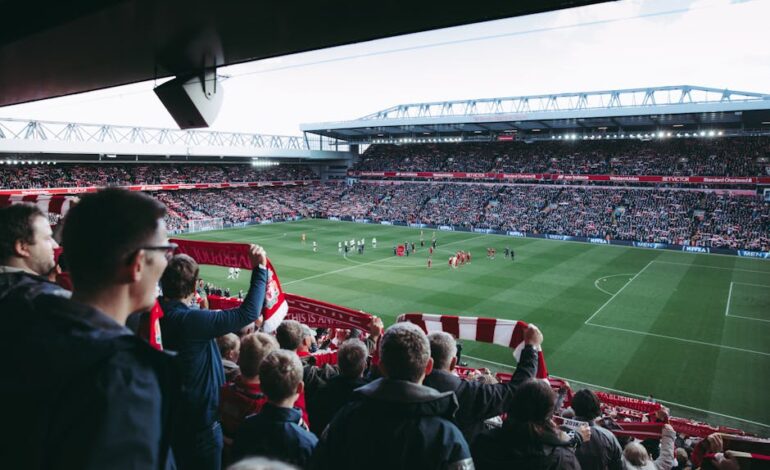 Fans cheer as players take the field at a vibrant football stadium, creating an electric atmosphere.