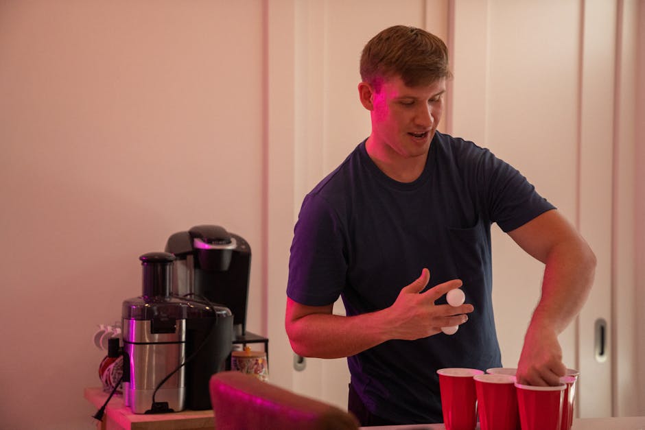 Man playing beer pong indoors with red cups and ping pong balls, enjoying recreation at home.