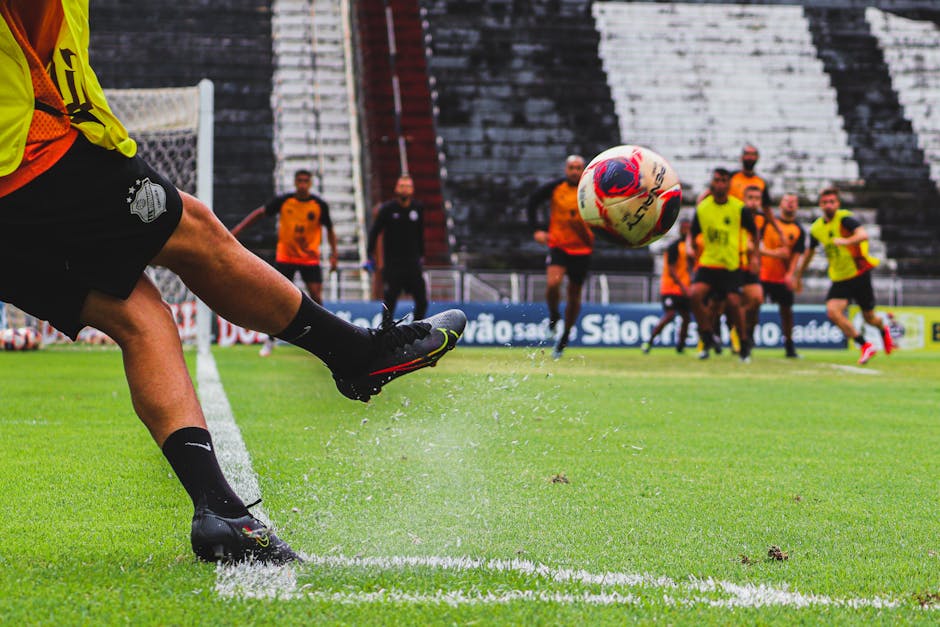 Male soccer player kicking ball on grass field during team practice session.