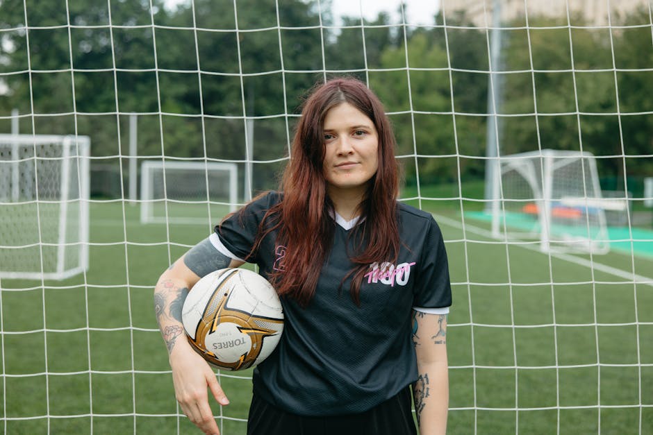 Young female soccer player posing with ball on outdoor field.