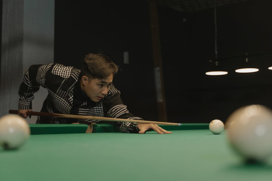 Young man aiming a cue in a billiards game under dim lighting.