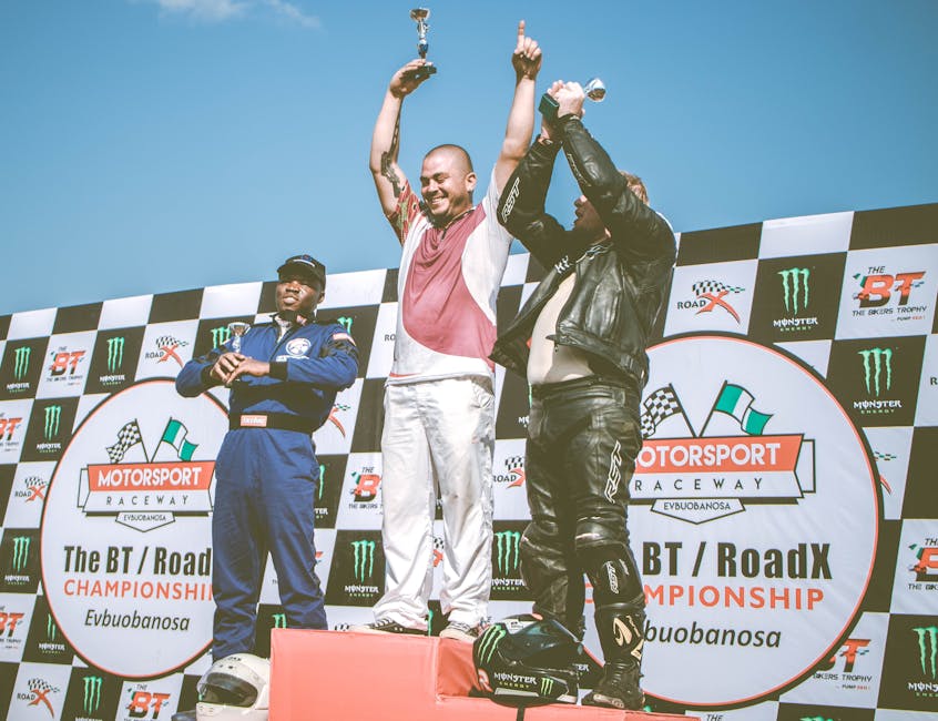 Three racers celebrate on the podium after a motorsport event, holding trophies.