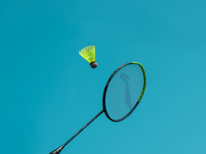 A thrilling action shot of a badminton racket hitting a shuttlecock against a clear blue sky.