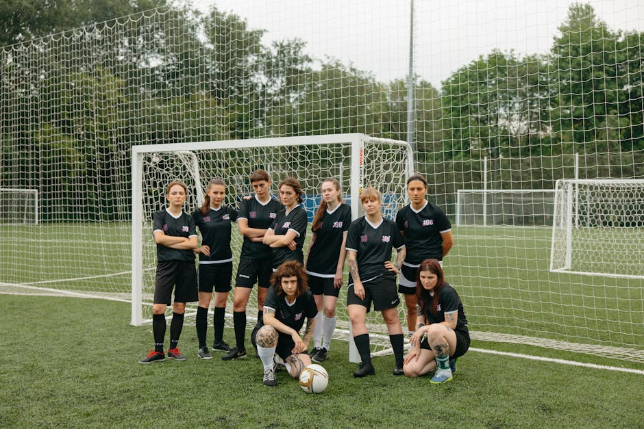 A diverse group of women soccer players pose confidently on a green soccer field.