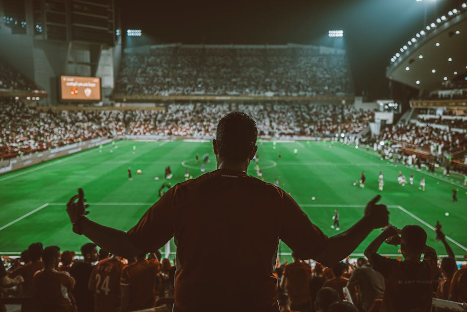Excited fans watch a thrilling football match at a packed stadium under bright lights.