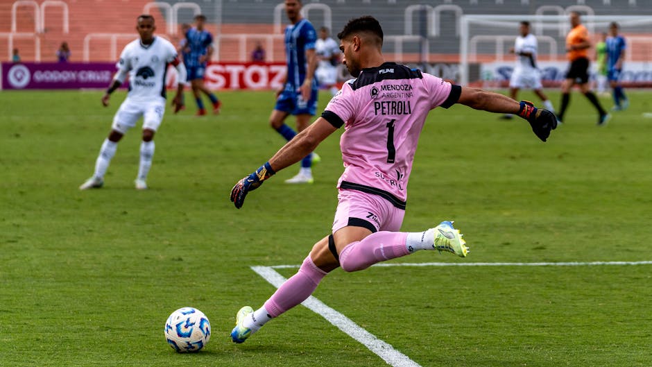Dynamic image of a soccer goalie kicking the ball during a match in a stadium.