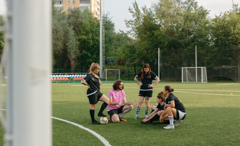 A mixed group of adults gathers on a sunny day for a team discussion on an outdoor football field.
