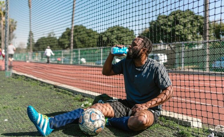 Soccer player resting by a field, hydrating after practice on a sunny day.