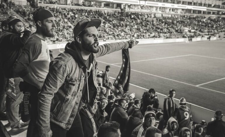 A crowd of passionate fans cheering during a soccer match in a packed stadium.