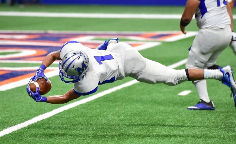 Football player making an incredible diving catch during a high-energy game in the stadium.