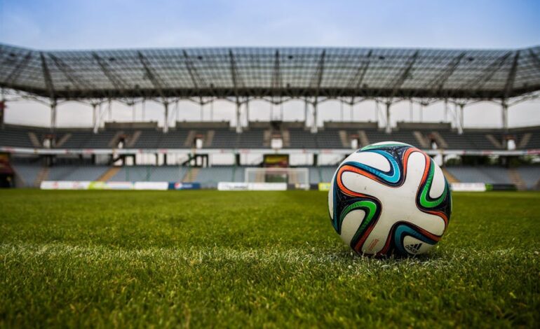 Close-up of a soccer ball on a lush grass field with an empty stadium in the background.