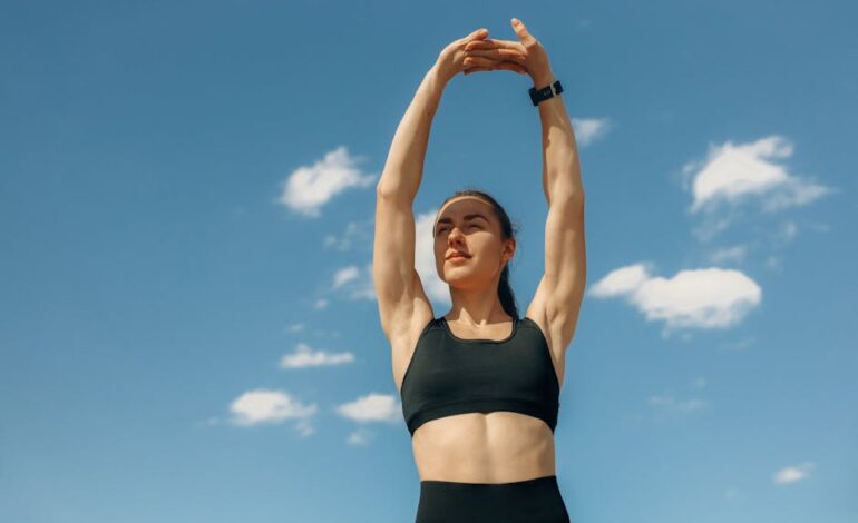 Woman in sports bra stretching under a clear blue sky, embodying fitness and wellness.