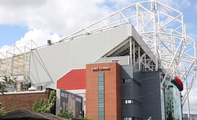 Exterior view of the East Stand at Old Trafford Stadium on a sunny day.