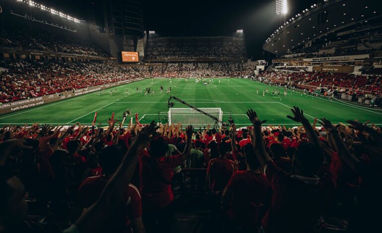Aerial view of a vibrant football match in a packed stadium at night, capturing the excitement of sports fans.