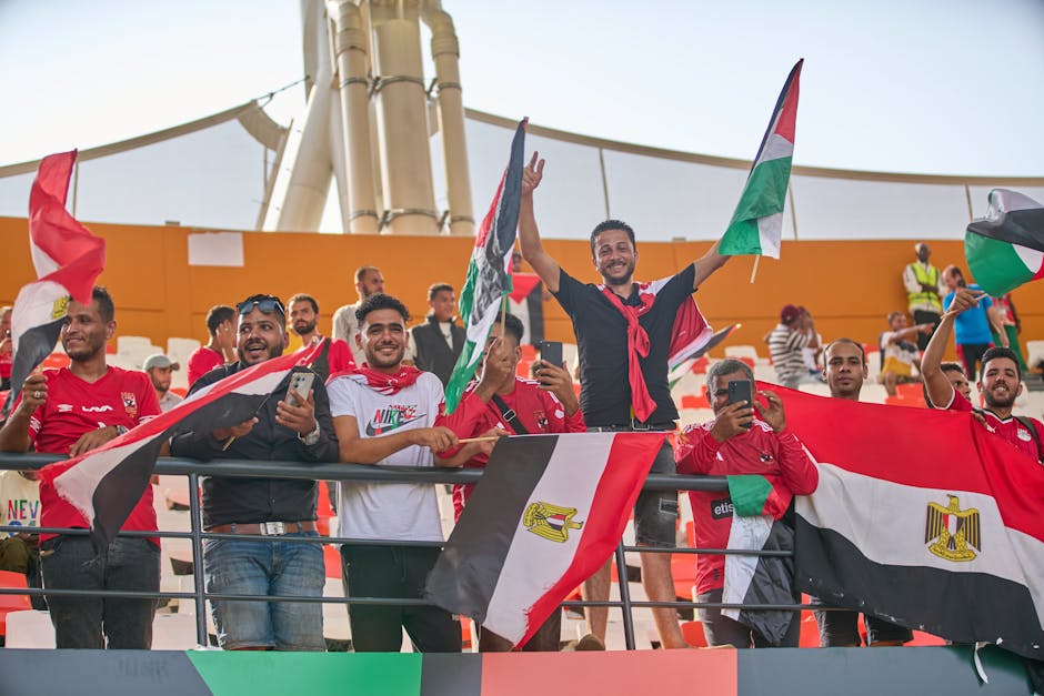 Group of enthusiastic soccer fans holding flags and cheering at a stadium event.