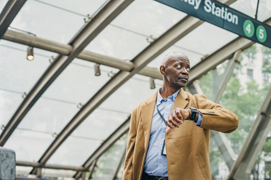 Serious African American businessman in formal clothes standing in subway station and checking time on wristwatch while looking away thoughtfully