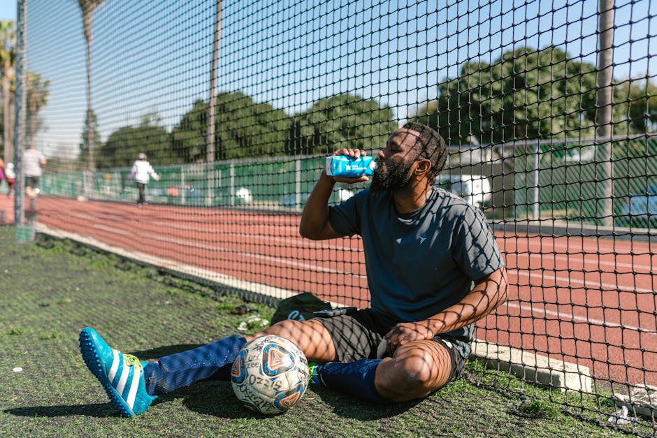 Soccer player resting by a field, hydrating after practice on a sunny day.