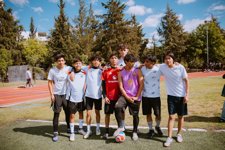 Group of teenagers posing together at a soccer field on a sunny day, showcasing team spirit and friendship.