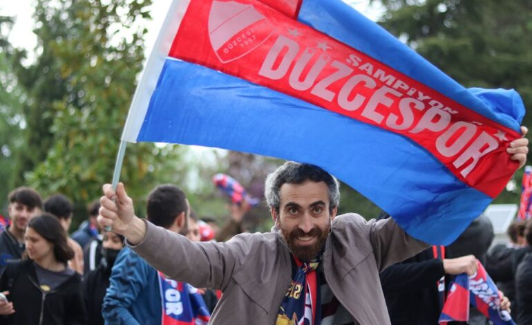 Excited Duzcespor supporters celebrate with flags outdoors, showcasing team spirit and joy.