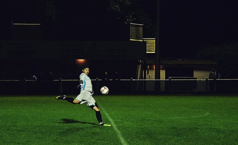 Dynamic action shot of a soccer player kicking the ball during a night game in Somerset, England.