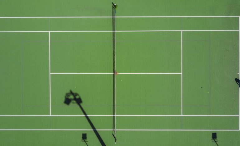 High-angle drone shot of a tennis match on a bright green court with shadows.