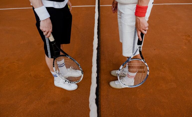Two tennis players stand on a clay court with rackets, ready for a match.
