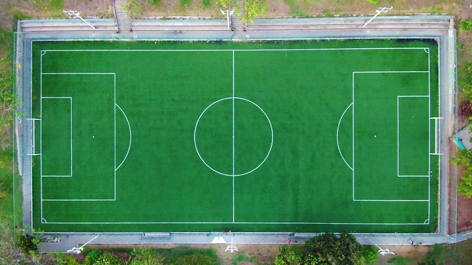 Bright aerial shot of an empty green soccer field with clearly marked lines.