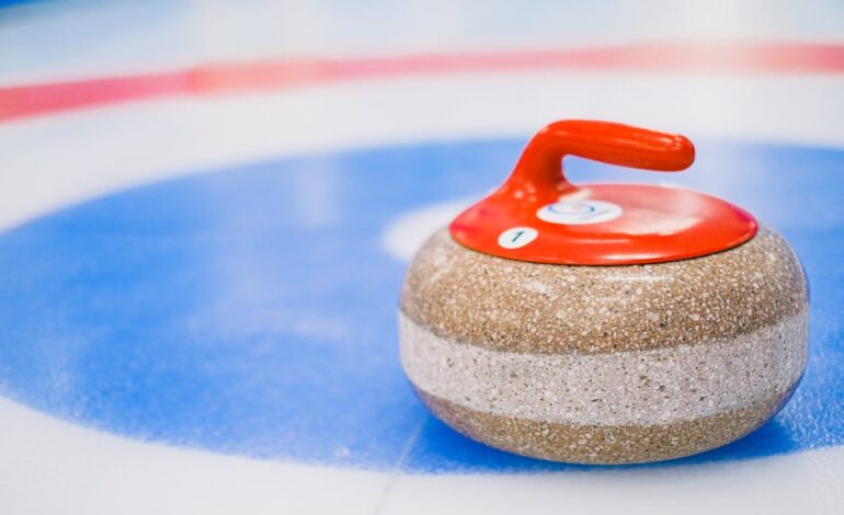 Round curling stone with red handle placed on ice surface on ice rink in daytime