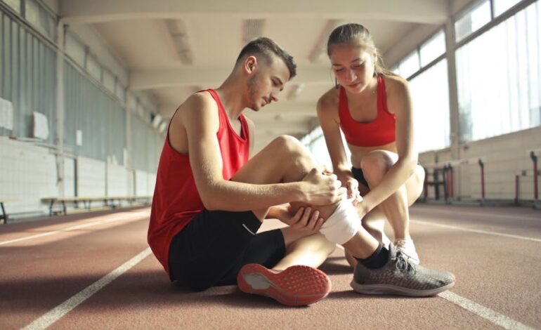 A woman helps an injured man's leg on an indoor track, providing first aid.