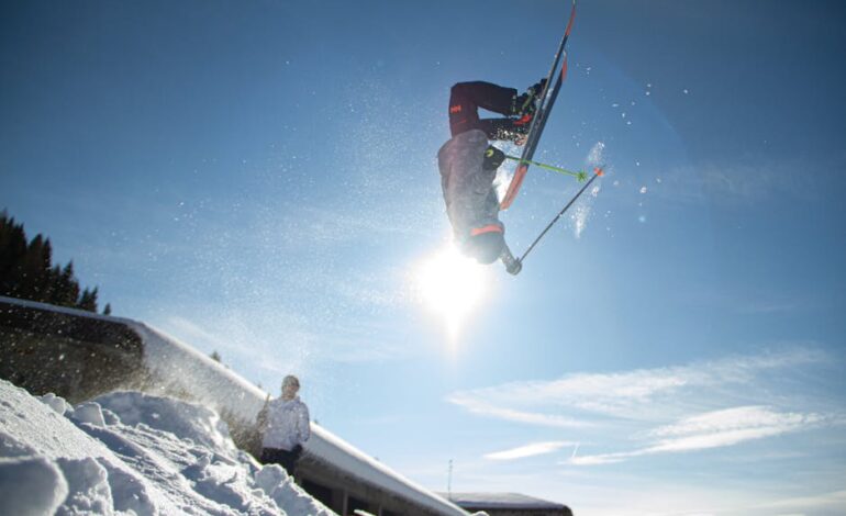 A skier performs a thrilling aerial stunt against a bright blue sky in the Italian Alps.
