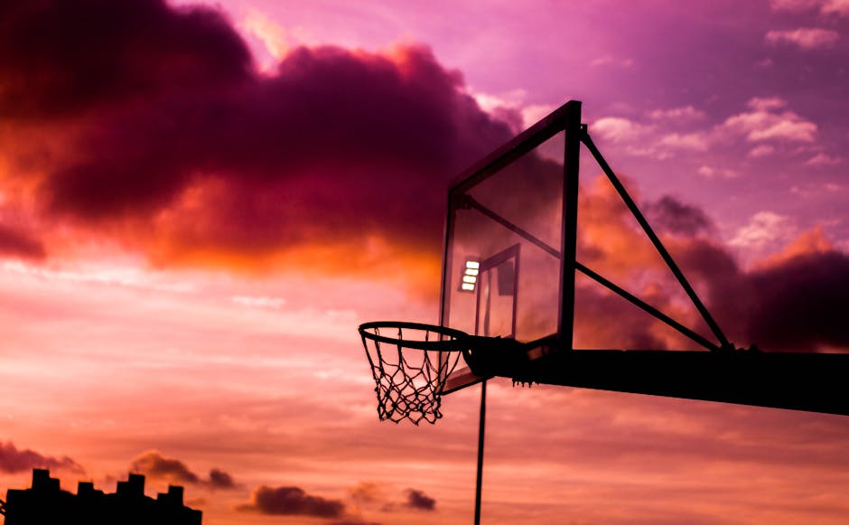 Silhouette of a basketball hoop against a vibrant orange and purple sunset sky.