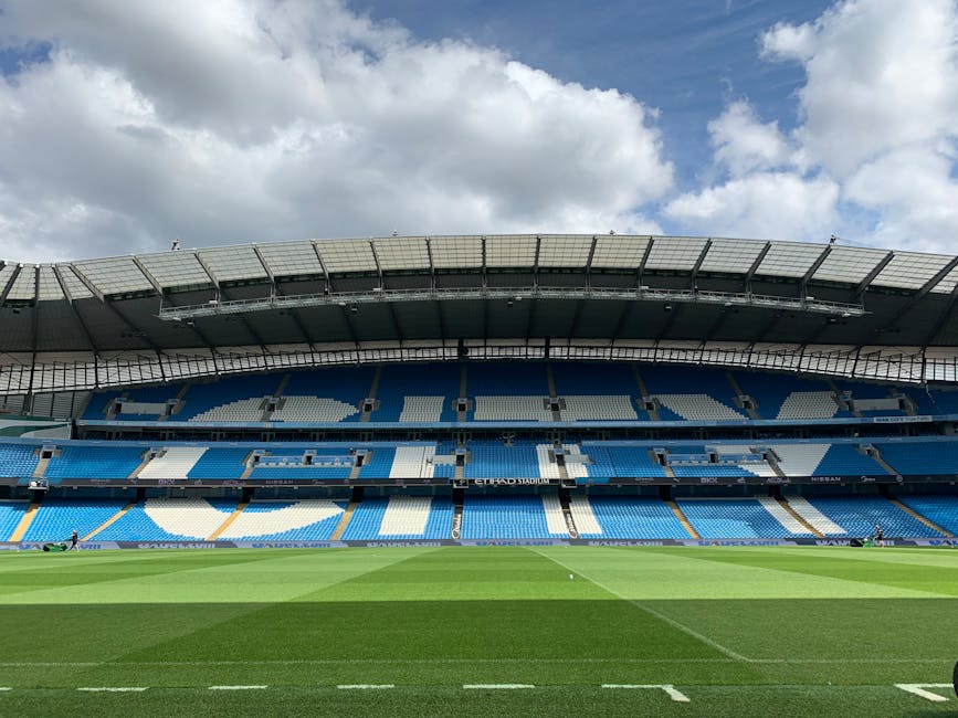 Etihad Stadium in Manchester with empty blue seats under a cloudy sky.