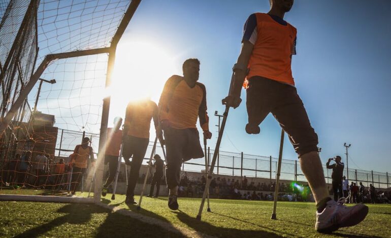 Amputee soccer players in orange jerseys competing on a sunny field.