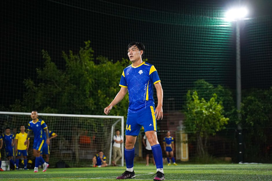 Soccer player in blue and yellow uniform during night game on a lit field.