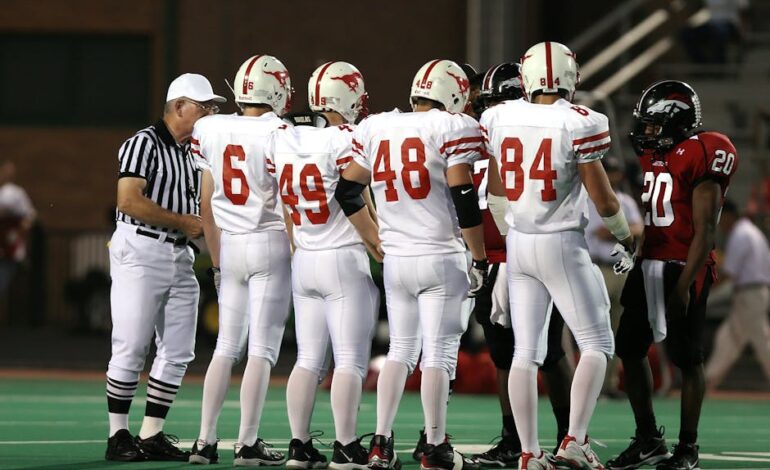 Exciting high school football teams in uniforms meet for a pre-game discussion under stadium lights.