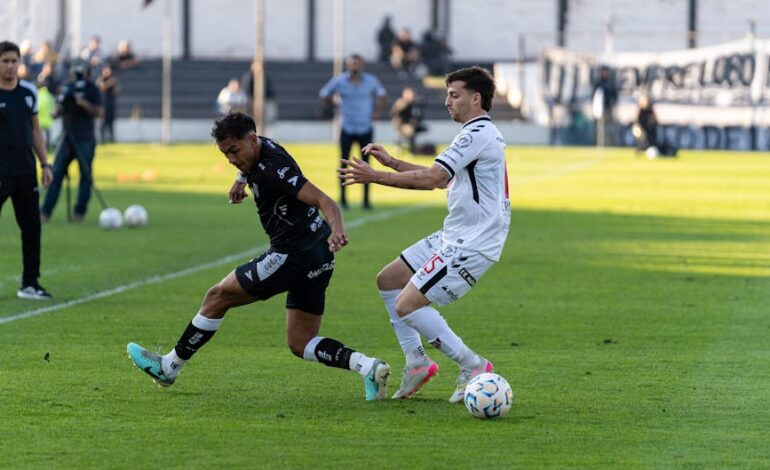 Intense action between two footballers competing in an outdoor match with clear daylight.