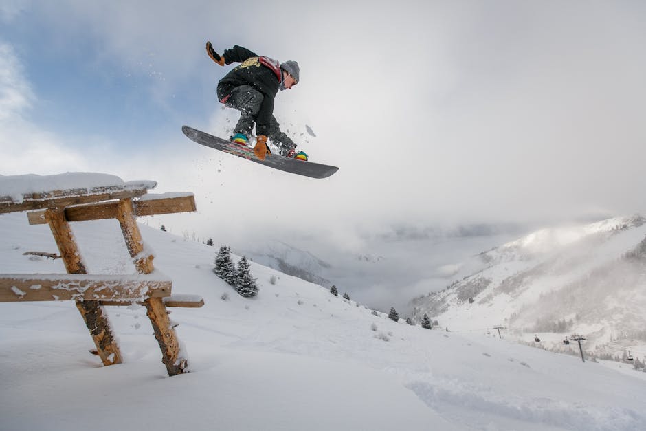 Snowboarder executing a jump over a snowy bench in a scenic winter mountain setting.