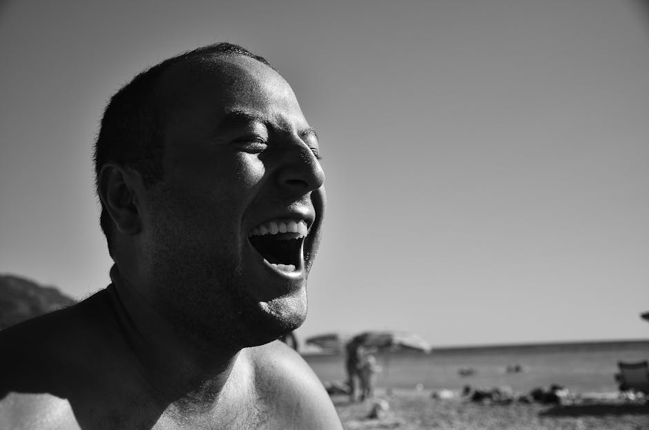 Black and white portrait of a man laughing at the beach during a sunny day.