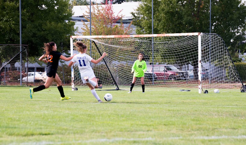 Women athletes competing in a lively soccer game with a goalkeeper defending the goal.