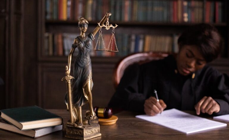 A focused judge writing on documents beside a Lady Justice statue in an office.