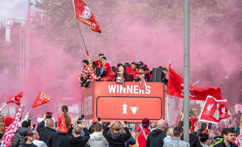 Celebratory parade in Liverpool with jubilant fans and players on an open-top bus.