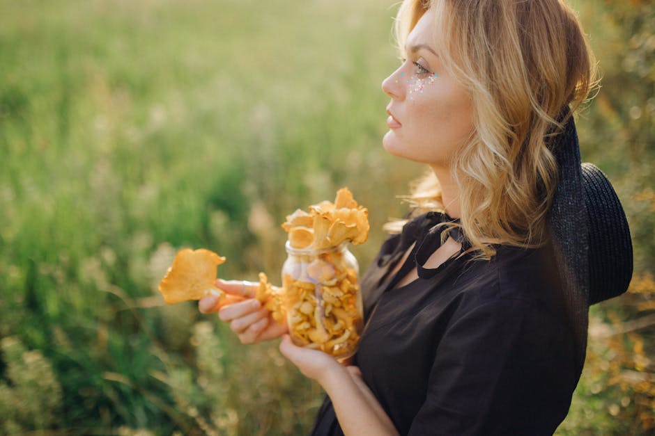 Young woman with blonde hair holding a jar of chanterelle mushrooms in a sunny, grassy field.