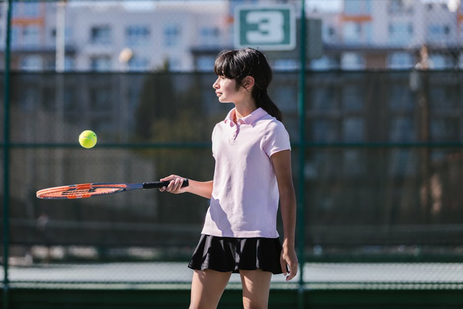 A young girl in activewear playing tennis on an outdoor court under the sun.