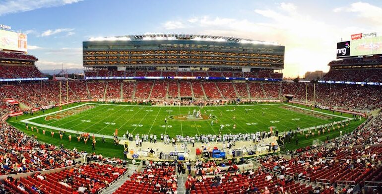 A stunning panoramic shot of Levi's Stadium in Santa Clara during a packed football game at sunset.